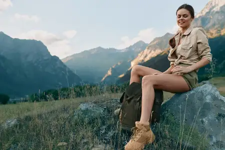 Непринужденный портрет женщины в походных ботинках и нейтральной одежде, наслаждающейся свежим воздухом и живописным диким пейзажем, передающий свободу, исследование и повседневное приключение