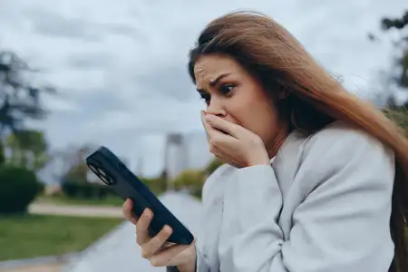 Взволнованная деловая женщина смотрит на свой смартфон в условиях открытого воздуха, выражая беспокойство