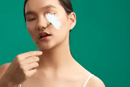 Азиатская женщина позирует с нежным цветком у лица на зеленом фоне