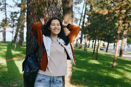Уличная сцена: улыбающаяся женщина у дерева в парке
