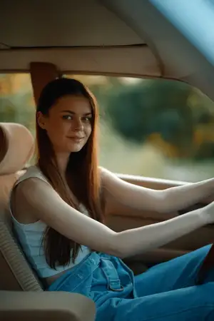 Молодая женщина с длинными волосами улыбается за рулем автомобиля