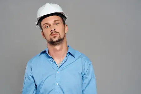 Мужчина в рабочей униформе и белой строительной каске выглядит профессионально и безопасно