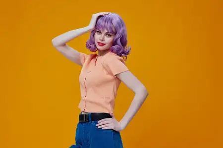Позитивная молодая женщина в стильной одежде, с макияжем и прической, позирует в студии, передавая эмоции