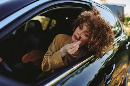Повседневный портрет женщины в автомобиле, поправляющей макияж