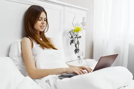 Симпатичная женщина с ноутбуком в постели и цветами, модель-фрилансер