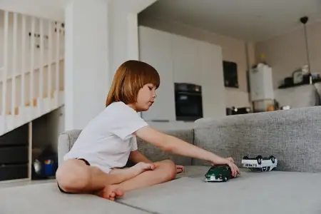 Маленький мальчик с энтузиазмом играет с игрушечными машинками на удобном диване в тепло освещенной гостиной, воплощая дух детской радости и воображаемой игры