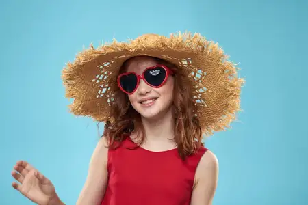 Девушка в соломенной пляжной шляпе и солнцезащитных очках, с кудрявыми волосами, на ярком синем фоне