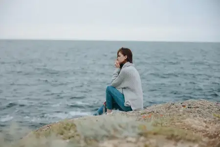 Женщина в свитерах на фоне облачного моря, любующаяся природой