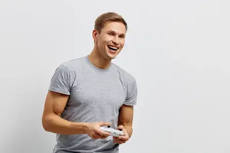 Счастливый молодой человек играет с контроллером, повседневная одежда, яркое жизнерадостное настроение, позитивная атмосфера, простой белый фон, демонстрирует досуг и развлечения, изображение образа…