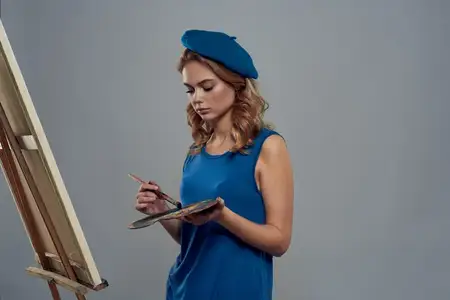 Женщина-художница в синем берете с палитрой рисует на мольберте