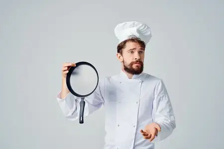 Бородатый мужчина-шеф-повар готовит на сковороде на кухне в сфере кулинарного искусства