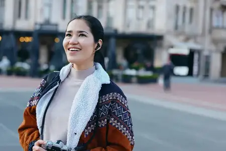 Счастливая женщина с камерой на оживленной городской улице, на ней теплая вязаная куртка и шарф