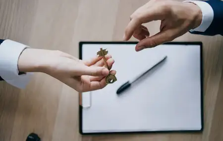 Передача ключа из рук в руки в офисе, на фоне документы по бизнесу и финансам