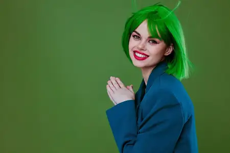 Симпатичная молодая девушка с привлекательным взглядом, в зелёном парике и синей куртке, позирует на зелёном фоне