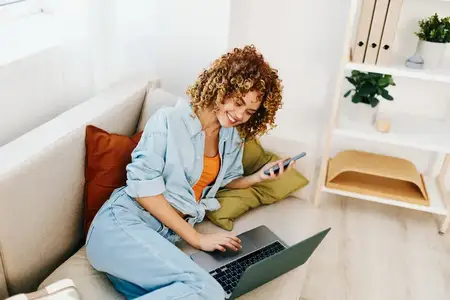 Улыбающаяся женщина работает за ноутбуком в уютной, современной гостиной