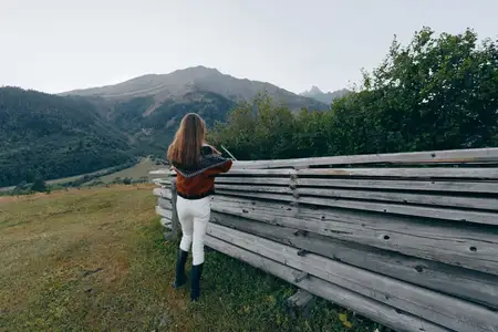 Женщина, забор, горы, сельская местность, луг, пейзаж природы, вид со спины человека в свитере и белых брюках, опирающегося на деревянный забор, наслаждающегося мирным пейзажем на открытом воздухе и…