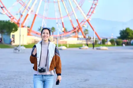 На уличной сцене изображена жизнерадостная женщина с фотоаппаратом перед колесом обозрения
