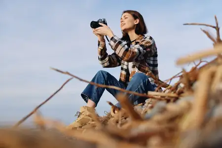 Портрет фотографа на открытом воздухе среди высокой травы, снимающего на камеру