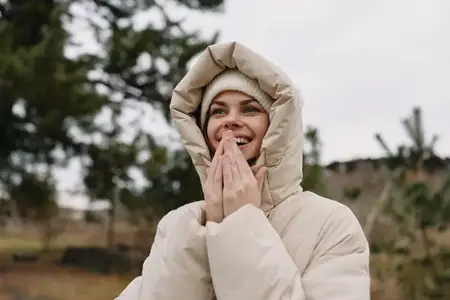 Молодая взрослая женщина в парке на улице, выражение надежды и радости, зимний пейзаж, облачное небо, спокойное настроение, защитная куртка, безмятежная природная обстановка