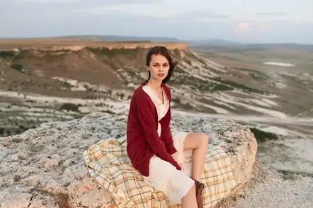 Женщина в красном кардигане и белом платье наслаждается величественным видом с вершины горы