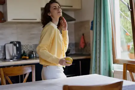 Яркая домашняя сцена с расслабленной женщиной в желтом кардигане на кухне: она наслаждается закуской и легким, непринужденным настроением