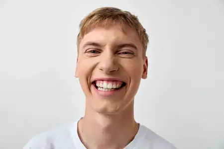 Радостный молодой человек с широкой улыбкой на чистом фоне, в повседневной футболке, с выразительным лицом и солнечным настроением