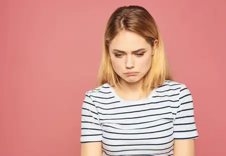 Расстроенная женщина с blond волосами на розовом фоне, одетая в модную футболку