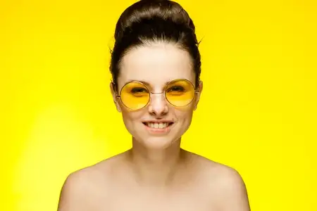 Женщина с обнаженными плечами в желтых очках на изолированном фоне