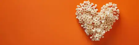 Форма сердца, созданная из мелких белых цветов на яркой оранжевой поверхности, передающая любовь и красоту