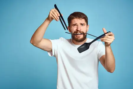 Бородатый мужчина с инструментами для приготовления пищи на голубом фоне, в белой футболке, лопатка