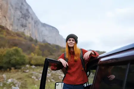 Женщина-туристка стоит рядом с автомобилем во время путешествия по горам на природе