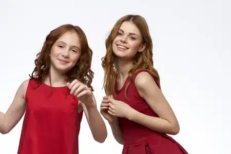 Весёлая мама и дочка в красных платьях обнимаются, демонстрируя жизнерадостный образ жизни на светлом фоне с улыбкой