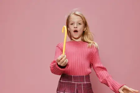 Счастливая школьница с розовым леденцом в студии, одетая в стильную одежду, выражающая радость и удивление