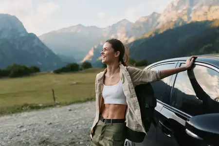 Яркая сцена: улыбающаяся женщина рядом с автомобилем на фоне суровых гор