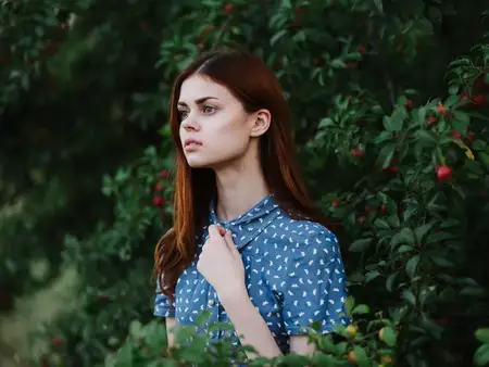 Женщина в синем платье стоит рядом с зелеными кустами в саду на природе