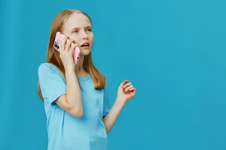 Маленькая девочка в светло-голубой рубашке держит розовый смартфон