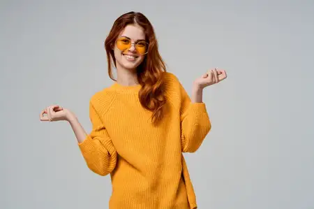 Красивая женщина в желтом свитере и модных очках на изолированном фоне