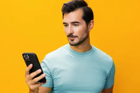 Мужчина в очках широко улыбается, показывая зубы, и держит смартфон, указывая на экран