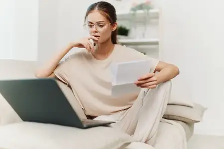 Улыбающаяся женщина работает за ноутбуком в уютной гостиной, используя современные технологии и наслаждаясь фриланс-работой