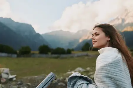 Крупный план той же женщины, смотрящей вдаль на фоне широкой долины и далеких вершин, подчеркивающий здоровье, заботу о себе, жизнь на природе и беззаботные путешествия