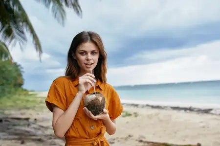 Женщина пьет кокосовый сок на острове у моря и пальм, экзотические тропики
