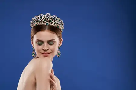 Принцесса с короной на голове, нанесённым макияжем, делает жест рукой на изолированном фоне