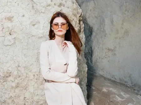 Красивая женщина в свитере стоит у скал на природе, на её лице очки