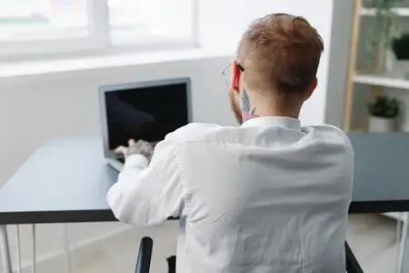 Мужчина в инвалидной коляске, бизнесмен с татуировками, работает в офисе за ноутбуком онлайн, социальные сети и стартап, интеграция в общество