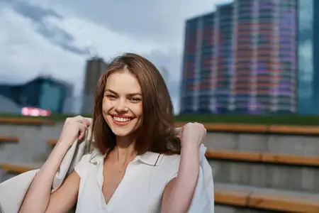 Уверенная женщина, одетая в шикарный деловой костюм, тепло улыбается на фоне современного городского пейзажа, воплощая расширение прав и возможностей и успех в профессиональной среде