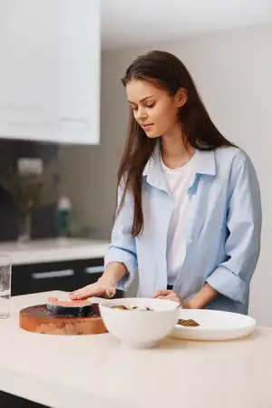 Молодая женщина стоит на кухне, рядом с ней на разделочной доске находятся миска с едой и стакан воды
