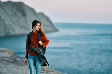 Женщина с рюкзаком, в свитере и джинсах, путешествует по горному пейзажу, модель