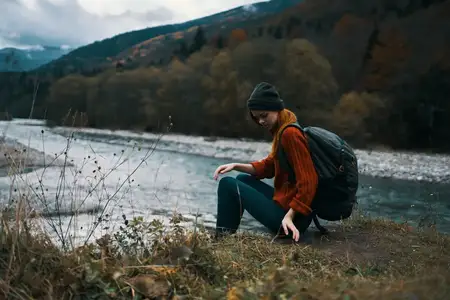 Женщина с рюкзаком за спиной наслаждается отдыхом на фоне гор и голубого неба, путешествуя по живописному ландшафту