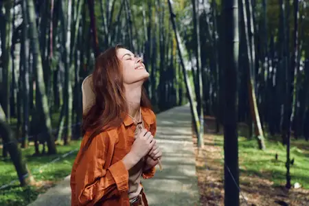 Женщина на лесной тропинке, счастье, природа, портрет на открытом воздухе, улыбается, наслаждаясь свежим воздухом, держа руки у груди