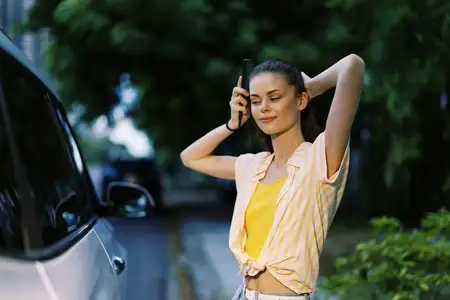 Молодая женщина стоит рядом с припаркованным автомобилем, улыбаясь и наслаждаясь моментом